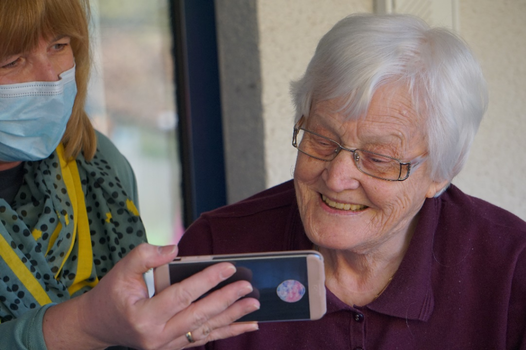 An older woman smiling at a smartphone screen.
